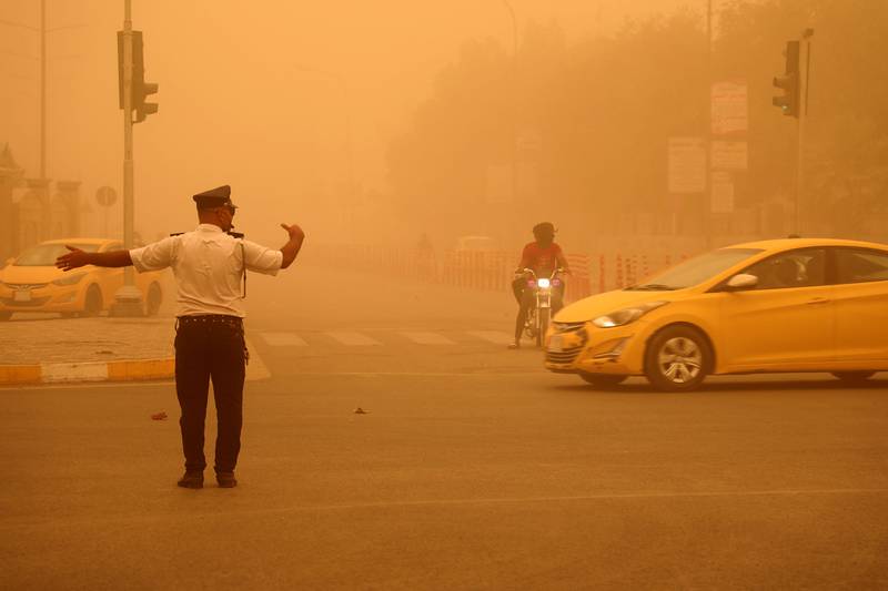 A traffic policeman directs the flow of cars as dust limits visibility in Nasiriyah. AFP