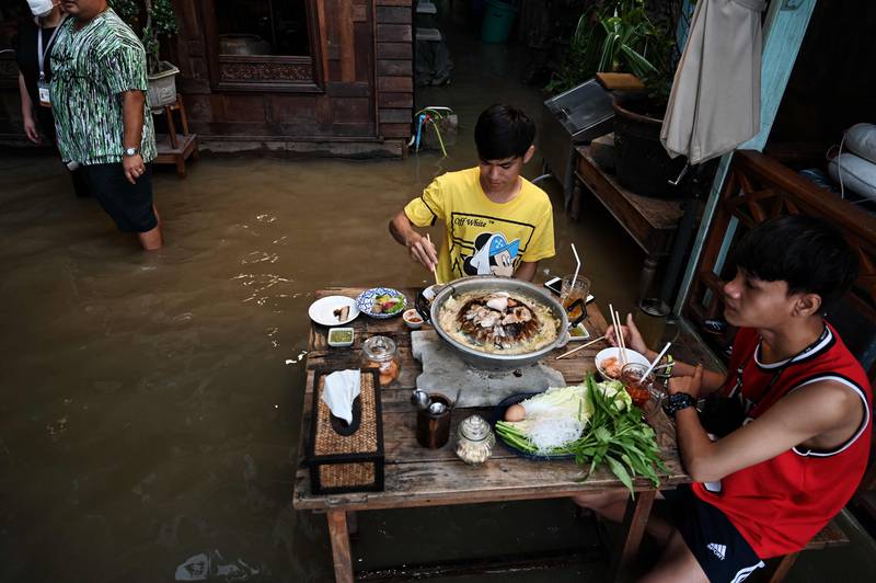 People eat dinner in a Bangkok restaurant as flood water from Thailand's Chao Phraya River surges in. AFP