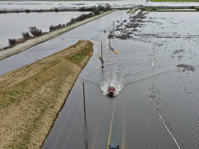 An aerial photograph shows a pickup truck pulling a trailer driving over a flooded road in the Central Valley during flooding from winter storms in Tulare County, near Alpaugh, California on March 22, 2023.  (Photo by Patrick T.  Fallon  /  AFP)