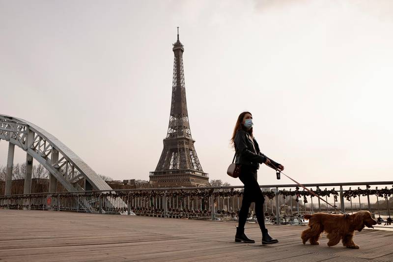 A woman, wearing a protective face mask, walks her dog on the Passerelle Debilly footbridge near the Eiffel tower in Paris, France. Reuters