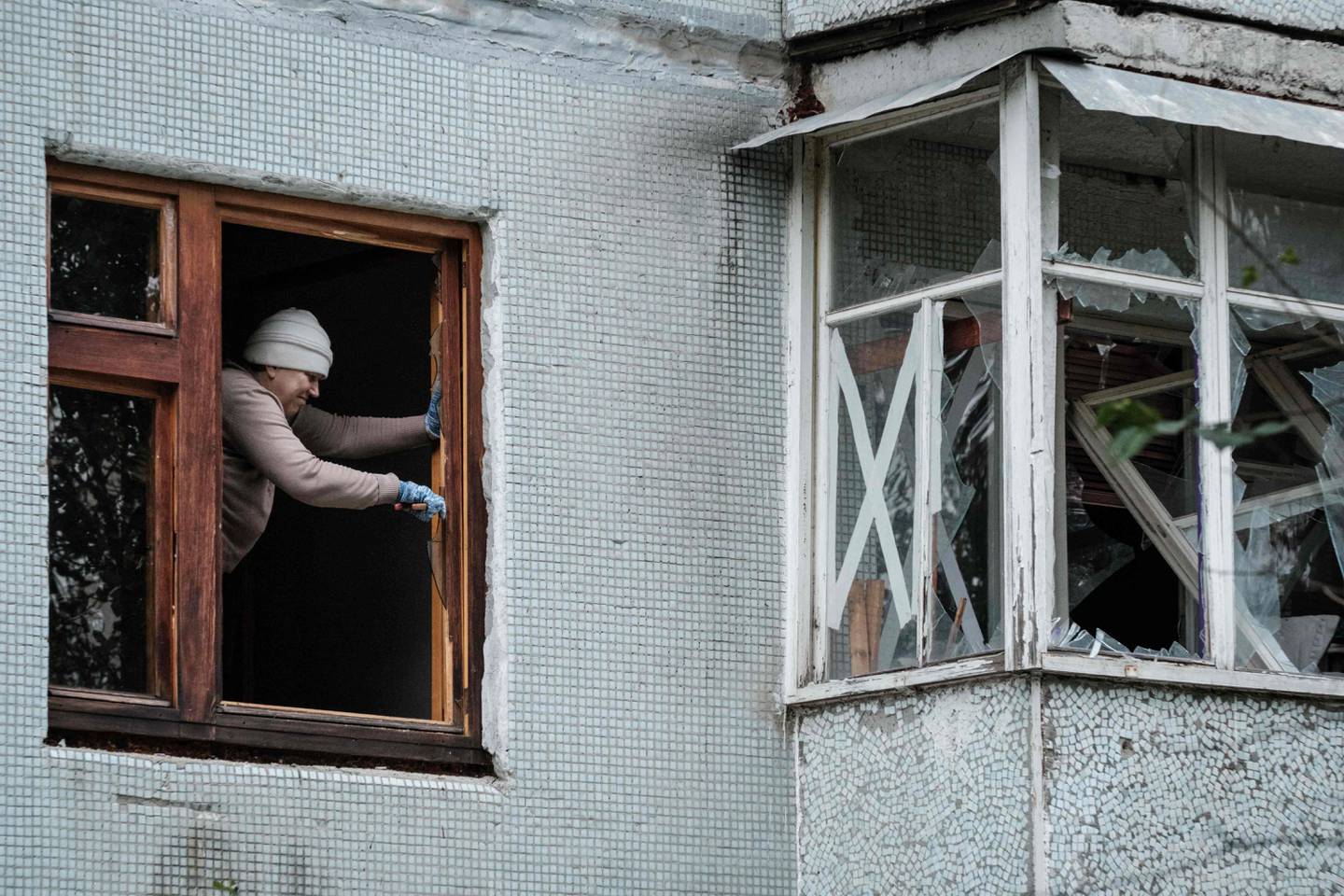 A woman removes a broken window at a building hit by a missile attack in Kharkiv. AFP