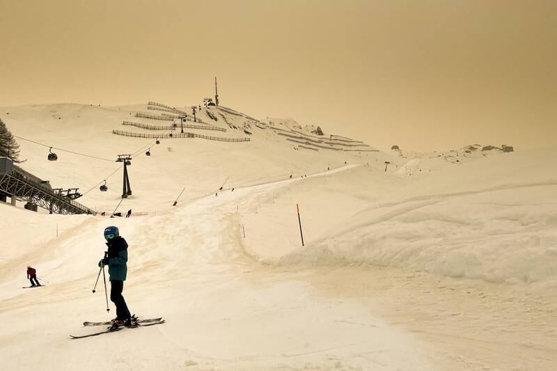 Skiers wearing protective face mask ski as Sahara sand colours the snow and the sky in a yellow cast and creates a special light atmosphere, in the Alpine resort of Anzere, Switzerland. EPA