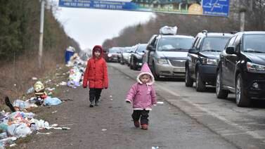 Ukrainian children walk past a line of cars heading towards the Polish border. AP