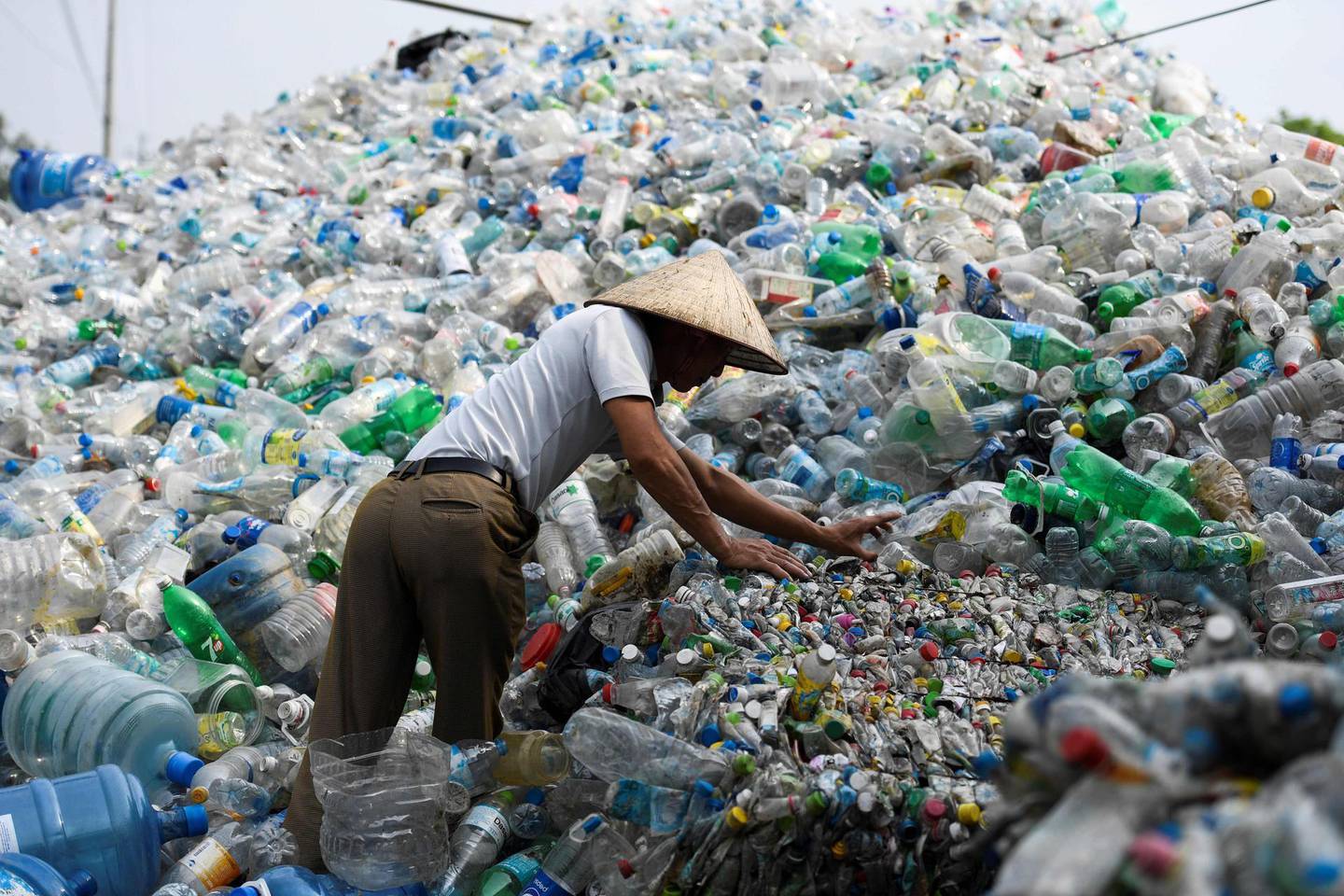 This picture taken on June 4, 2018 shows a man sorting through used plastic bottles at a junkyard in Hanoi. About eight million tonnes of plastic waste are dumped into the world's oceans every year - the equivalent of one garbage truck of plastic being tipped into the sea every minute... of every day. Over half comes from five Asian countries: China, Indonesia, the Philippines, Thailand and Vietnam, according to a 2015 study in Science journal. / AFP / Nhac NGUYEN
