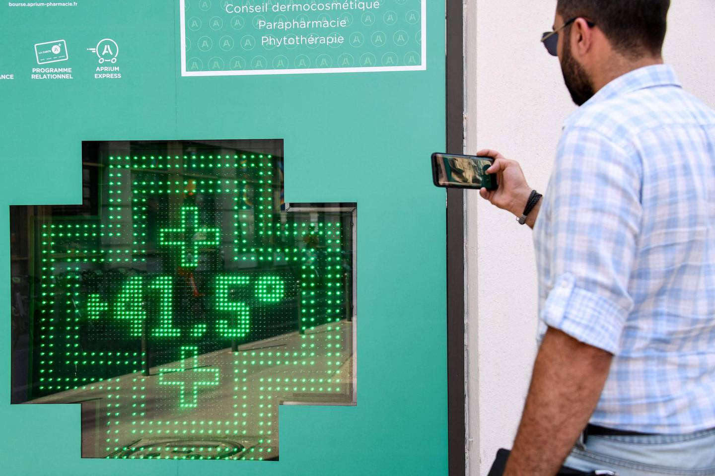 (FILES) In this file photo taken on July 25, 2019, a pedestrian takes a photograph of a  thermometer display showing a temperature of 41,5 degrees Celsius on the exterior of a pharmacy in Paris, as a new heatwave hits northern Europe. The new novel from sci-fi writer Kim Stanley Robinson opens with an unrelenting heatwave in northern India that leaves the reader gasping for air just like the millions of people desperately trying to stay cool enough to survive. The scene described and its grim outcome may be closer to science than fiction, according to the revised draft of a landmark report from the UN's climate science advisory panel obtained by AFP. / AFP / Bertrand GUAY
