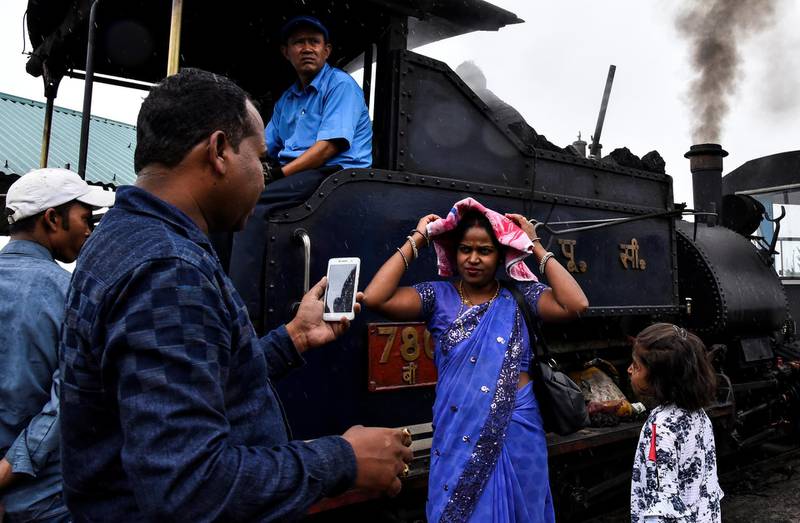 Passengers stand next to a Darjeeling Himalayan Railway steam train as it halts briefly at Batasia Loop.