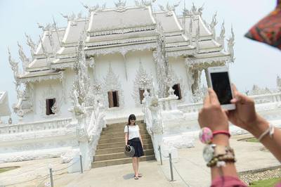 A tourist posing for a picture as she visits the White Temple in Chiang Rai, northern Thailand. Accused of urinating in public, spitting on the street, or kicking a sacred temple bell, free-spending Chinese tourists are receiving a mixed welcome as their soaring numbers help the kingdom's creaking economy.  Christophe Archambault/AFP Photo