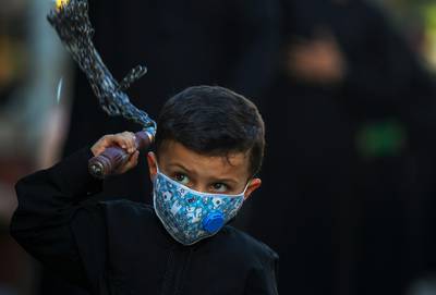 An Iraqi boy, wearing a protective mask, beats himself with chains during a procession in Baghdad's northern district of Kadhimiya, ahead of the 10th day of Muharram, which is celebrated as Ashura.  AFP