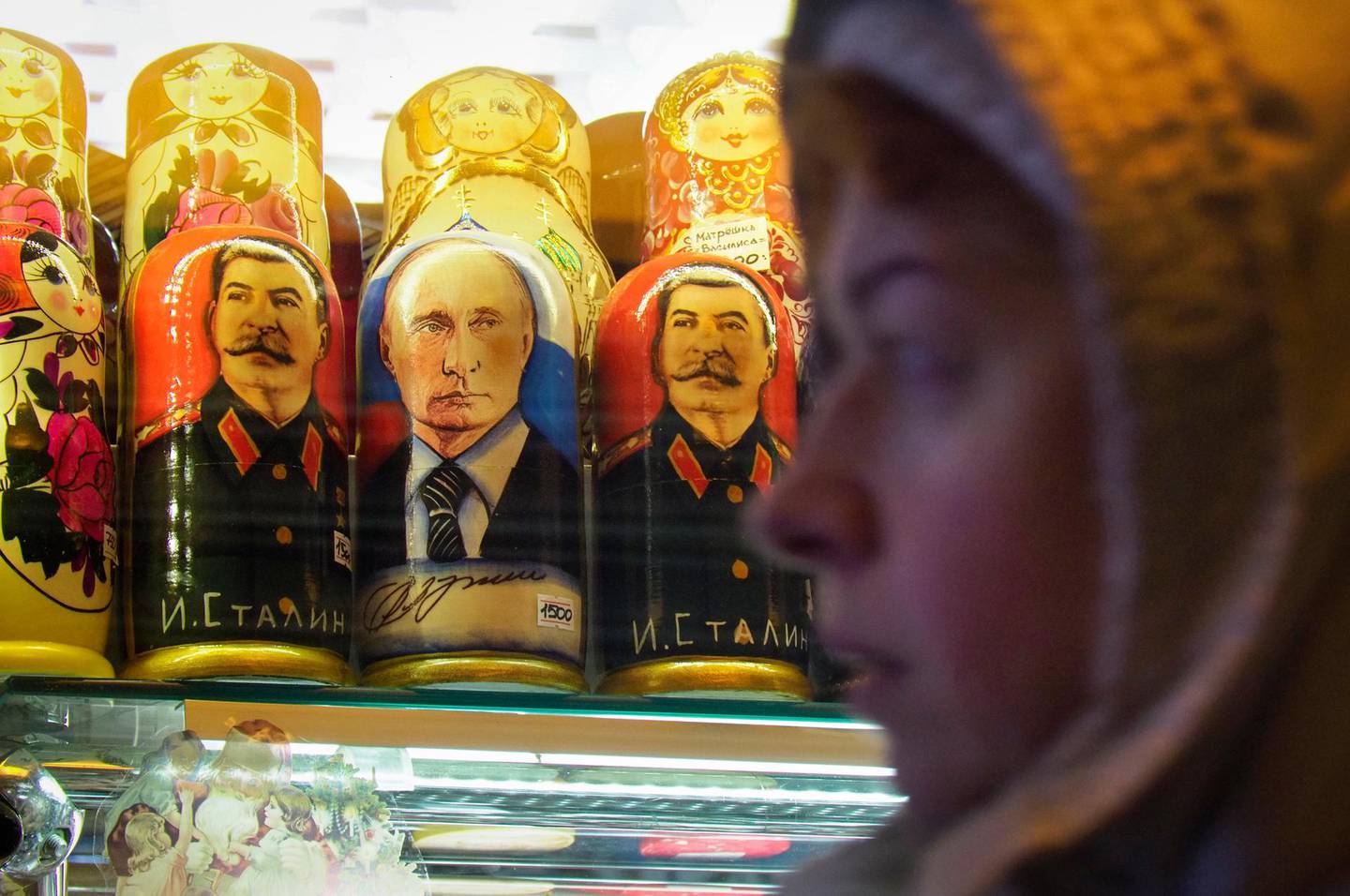 A woman walks past traditional Russian wooden dolls called Matryoshka depicting Russian President Vladimir Putin and Josef Stalin, displayed for sale at a souvenir street shop in St. Petersburg, Russia, Saturday, Dec. 28, 2019. (AP Photo/Dmitri Lovetsky)