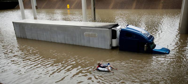 After helping the driver of the submerged truck get to safety, a man floats on the freeway flooded by Hurricane Harvey near downtown Houston.  Charlie Riedel / AP Photo