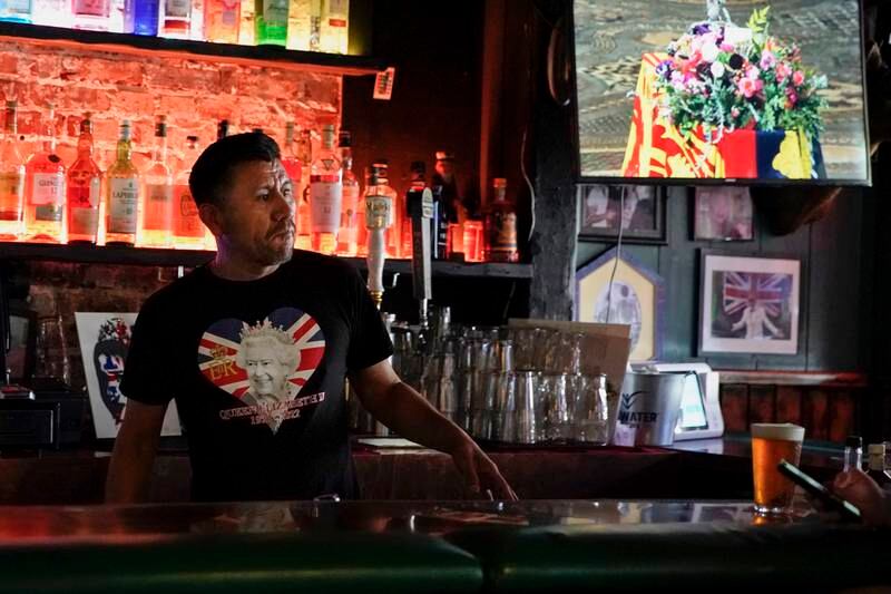 Leon Lopez wears a commemorative Queen Elizabeth shirt as he stands behind the bar at Ye Olde King's Head. EPA