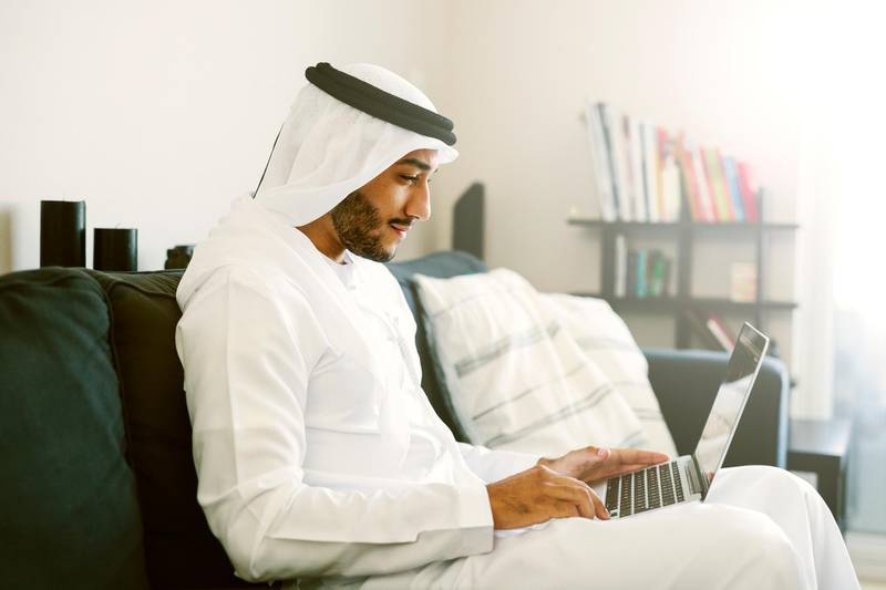 Middle eastern man at home. Sitting on a couch and using laptop. Backlight and sunflare.