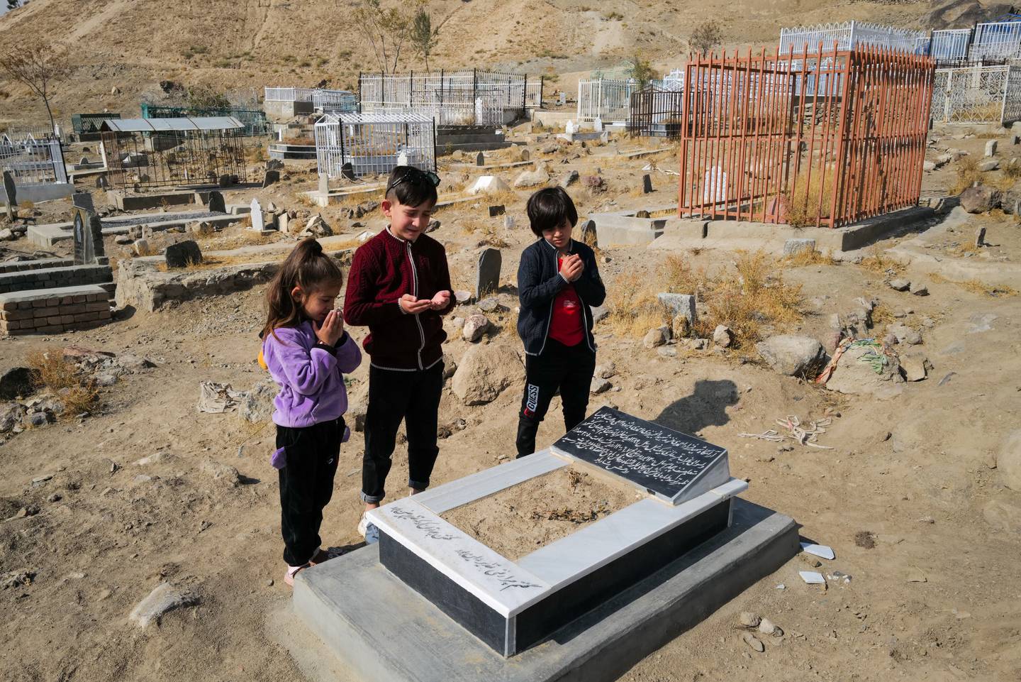 Ada Ahmadi stands with her cousins as they pray by the grave of their relative Farzad, who was a victim of a US drone strike that killed 10 civilians, including seven children, in Kabul, Afghanistan, on November 7, 2021. Reuters