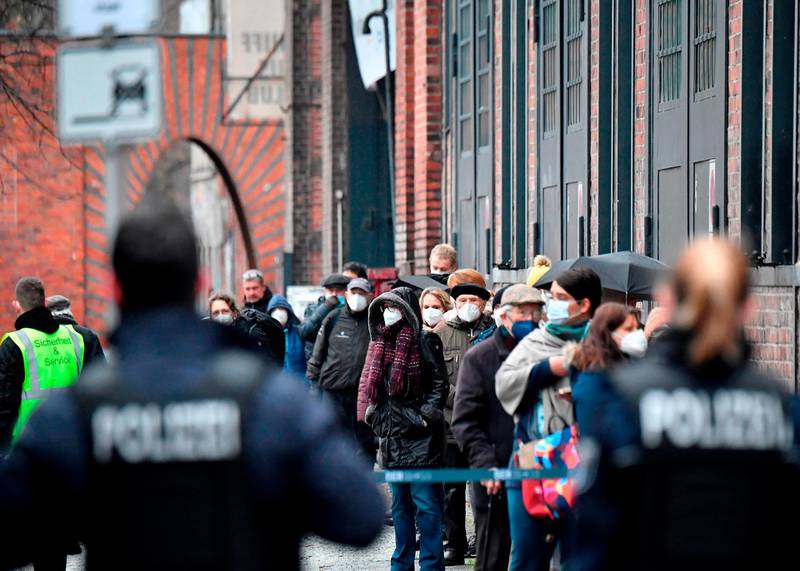 Police stand by as people wearing face masks queue to get access to the vaccination center at the 'Arena' in Berlin's Treptow district in Germany. AFP