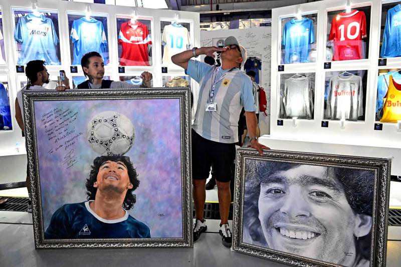 A fan stands next to paintings of Diego Maradona painted by Argentine artist Claudia Perez, on the second anniversary of Maradona's death at a fan zone devoted to the Argentine at Doha's international airport on November 25, 2022. AFP