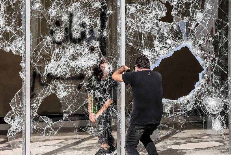 A protester poses for a photo behind smashed glass and slogan reading in Arabic 'Lebanon only' during students protest in Beirut on November 12, 2019.  EPA