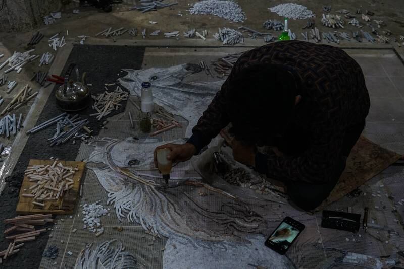 A worker colours a horse on a mosaic that is almost ready.