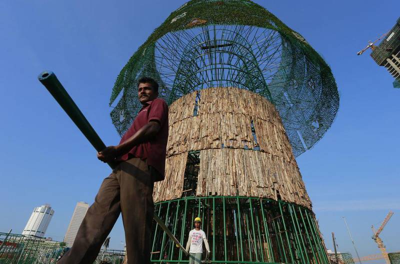 In this Thursday, Dec. 15, 2016 photo, Haloluwage Don Nanayakkara, left, carries a steel rod with another worker as they try to build an enormous, artificial Christmas tree on a popular beachside promenade in Colombo, Sri Lanka. The idea for the tree came from this Buddhist driver at Colombo‚Äôs port who makes decorations in his spare time. Hundreds of Sri Lanka‚Äôs port workers and volunteers are struggling to put up the towering Christmas tree in time for the holidays. The majority-Buddhist nation is aiming to beat the world record for the tallest, artificial Christmas tree as a show of multicultural respect. But twice the construction deadline was missed, and now organizers hope to erect the tree on Christmas Eve. The Catholic Church has criticized the $80,000 price tag as a waste of money that is better spent helping the poor. (AP Photo/Eranga Jayawardena)