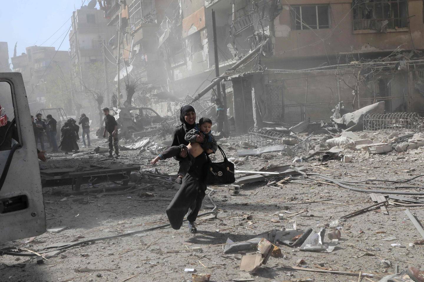 TOPSHOT - A Syrian woman holds a child and runs for cover following Syrian government air strikes on the Eastern Ghouta rebel-held enclave of Douma, on the outskirts of the capital Damascus on March 20, 2018.
Syrian regime and allied forces battled to suppress the last pockets of resistance in and around Damascus while the beleaguered Kurds in the north braced for further Turkish advances. Assad has in recent months brought swathes of territory back under his control thanks to heavy Russian involvement, as well as support from other forces such as the Iran-backed Lebanese Hezbollah militia. Eastern Ghouta's main town of Douma remains under rebel control but even as a trickle of emergency medical evacuations was scheduled to continue, the regime continued to pound the enclave. / AFP PHOTO / HAMZA AL-AJWEH