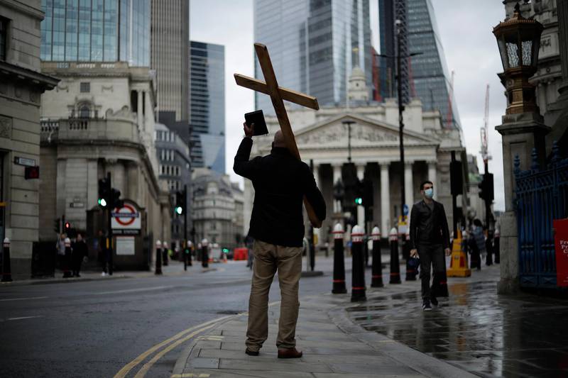 A man holding a cross and a Bible preaches about Christianity backdropped by the Royal Exchange, back centre, and the Bank of England, at left, during England's second coronavirus lockdown in the City of London. AP Photo