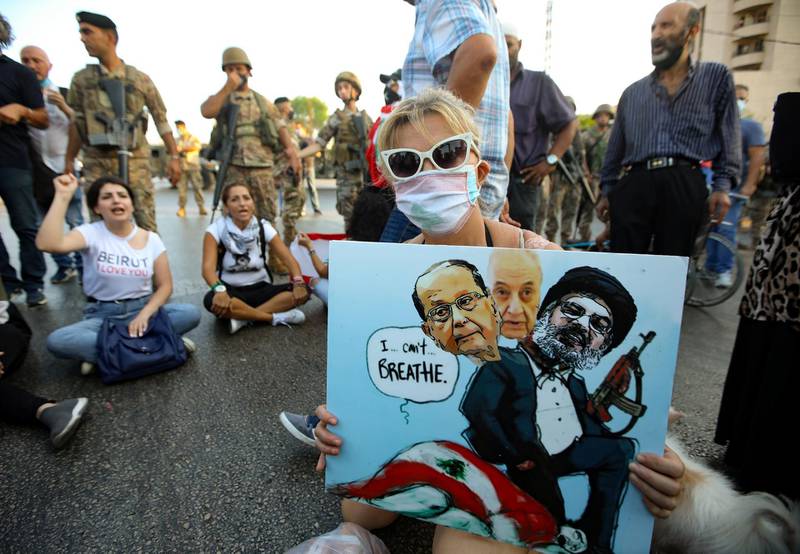 A Lebanese anti government protester holds a placard with a cartoon of (L-R) President Michel Aoun, Parliament Speaker Nabih Berri and  head of the Shiite movement Hezbollah Hassan Nasrallah sitting atop a national flag (with writing that refers to George Floyd's death) during a demonstration against the lack of progress in a probe by authorities into a monster blast that ravaged swathes of the capital 40 days ago, near the presidential palace in Baabda, east of the capital Beirut, on September 12, 2020. (Photo by ANWAR AMRO / AFP)