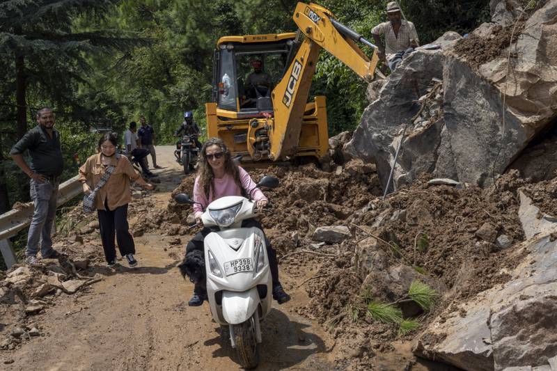 A woman and her dog on a scooter ride past an earthmover clearing a road of a big rock that came down with mud and plant debris following intense monsoon rains in Dharmsala, Himachal Pradesh, India, on August 21. AP