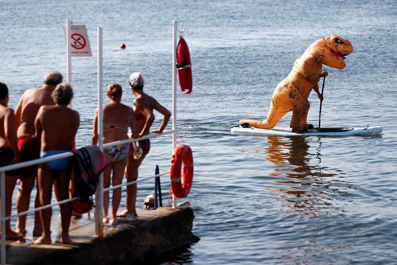 People look at a man wearing a T-Rex costume on a paddle board during hot weather at Sferracavallo beach, following the outbreak of the coronavirus disease (COVID-19) in Palermo, Italy, July 31, 2020. REUTERS/Guglielmo Mangiapane
