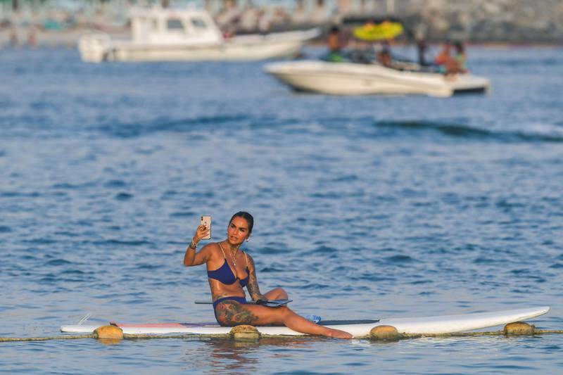 A woman athlete uses a phone as she sits on a surfboard during the Dubai watersport festival, organised by the Dubai International Marine Club (DIMC), near the Burj Khalifa skyscraper in the Gulf emirate on June 25, 2020.  / AFP / KARIM SAHIB
