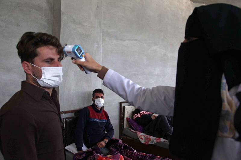 A health worker measures the temperature of a man at a quarantine facility for Syrians who returned from Turkey in the countryside of the town of Jisr al-Shughur, west of the mostly rebel-held Syrian province of Idlib, on April 27, 2020 amid the coronavirus COVID-19 pandemic. / AFP / Abdulaziz KETAZ
