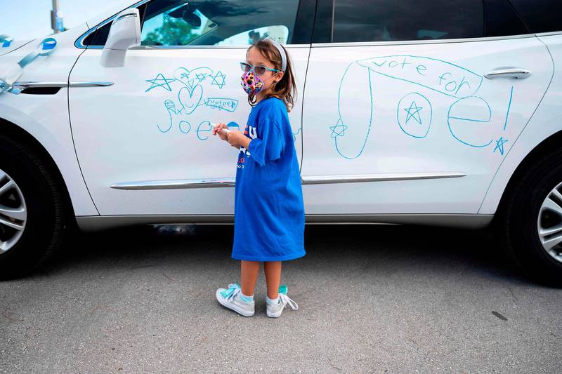 Seven-year-old supporter Lexi Katzman draws campaign slogans on her father's car as Democratic Presidential candidate and former US Vice President Joe Biden delivers remarks at a Drive-in event in Coconut Creek, Florida, on October 29, 2020.  AFP