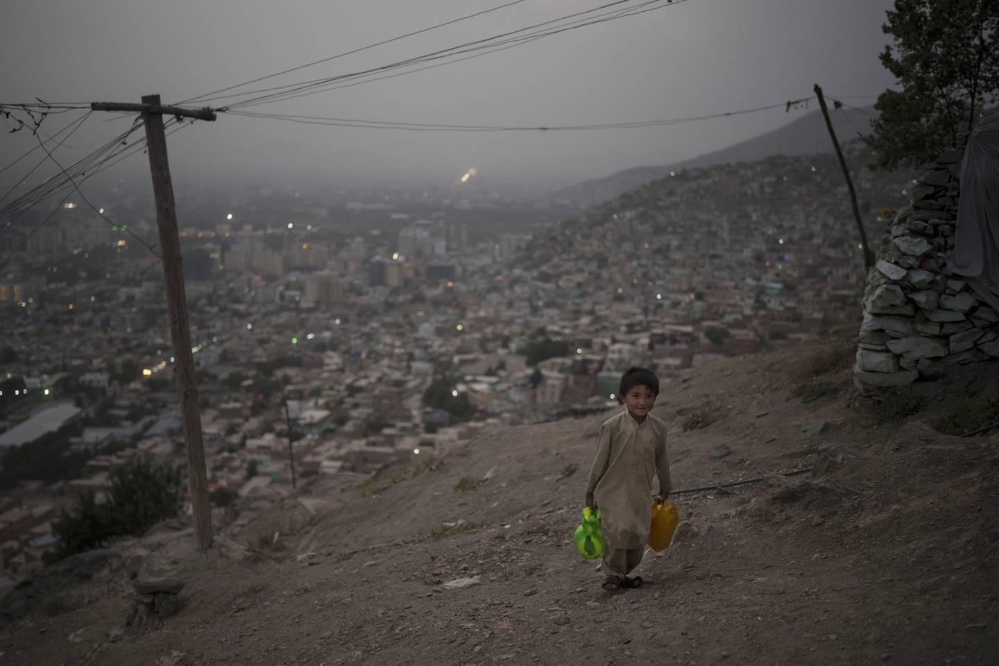 A boy trudges up a hill to his home, carrying bottles of water in Kabul, Afghanistan. AP Photo