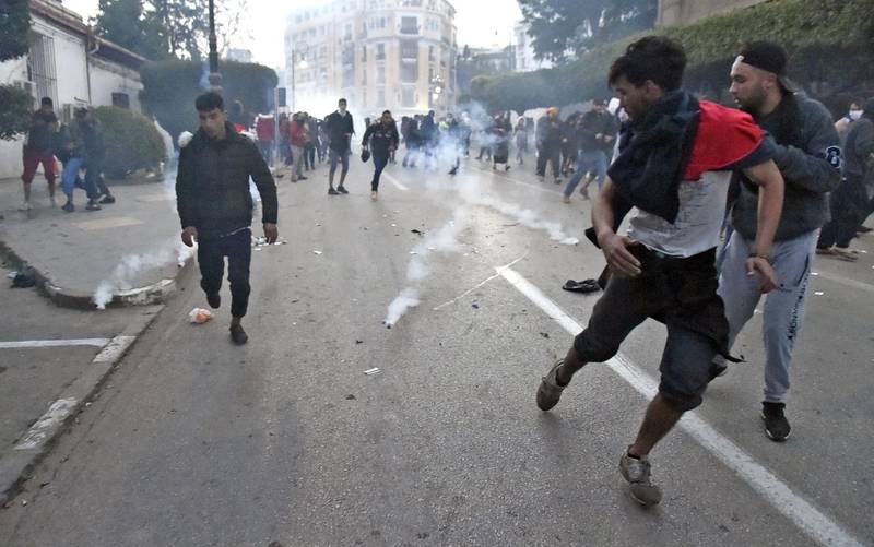 Algerian protesters running in a street as police in riot gear fired tear gas and set up a security cordon to block access to the presidential palace. AFP