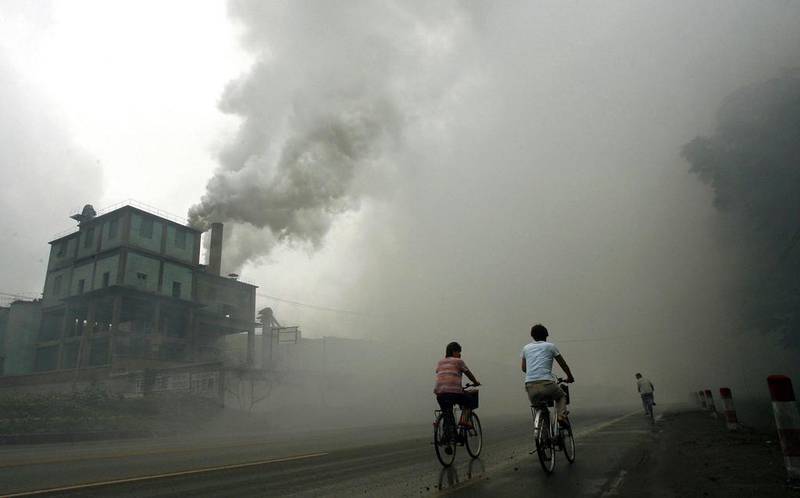 Cyclists pass through thick pollution from a factory in Yutian in China's northwest Hebei province. AFP 