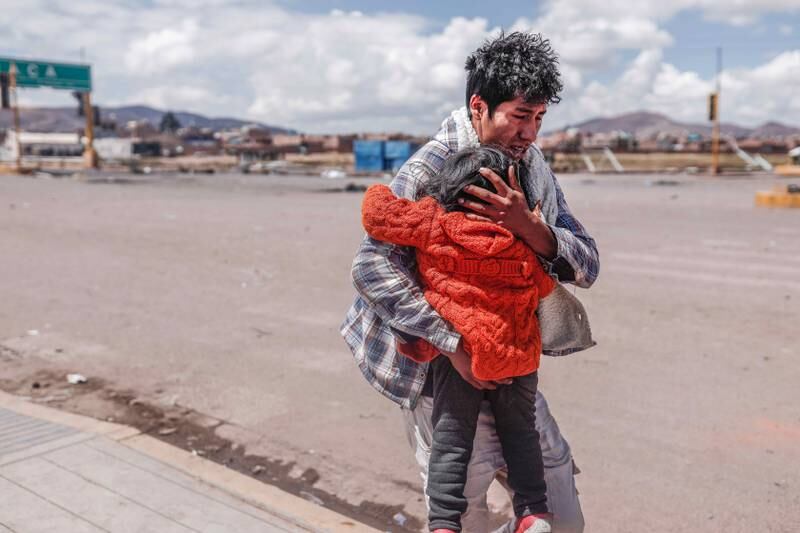 A man shields a child as he runs for cover during protests near Juliaca airport in Peru. Demonstrations against the government of Dina Boluarte left at least 12 injured on Friday. EPA