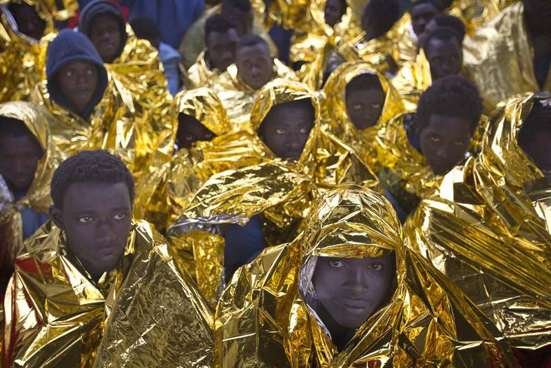 Wrapped in blankets, sub-Saharan migrants sit on the deck of the Golfo Azzurro rescue vessel after arriving at the port of Messina, in Italy, with more than 299 migrants aboard the ship rescued by members of Proactive Open Arms NGO. Emilio Morenatti / AP Photo