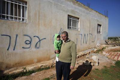 Palestinian Hussein Al Najjar Darwish holds his nine-month-old son as she stands in front of his house sprayed with graffiti reading in Hebrew: "revenge" and "hello from the prisoners of Zion", in the village of Beitillu, near Ramallah in the Israeli occupied West Bank on December 22. Abbas Momani / AFP Photo
