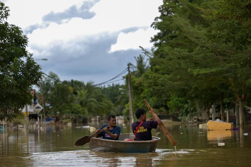 Residents ride a boat through floodwaters in Mentakab in Malaysia's Pahang state on January 8, 2021, following heavy monsoon rains. / AFP / Mohd RASFAN
