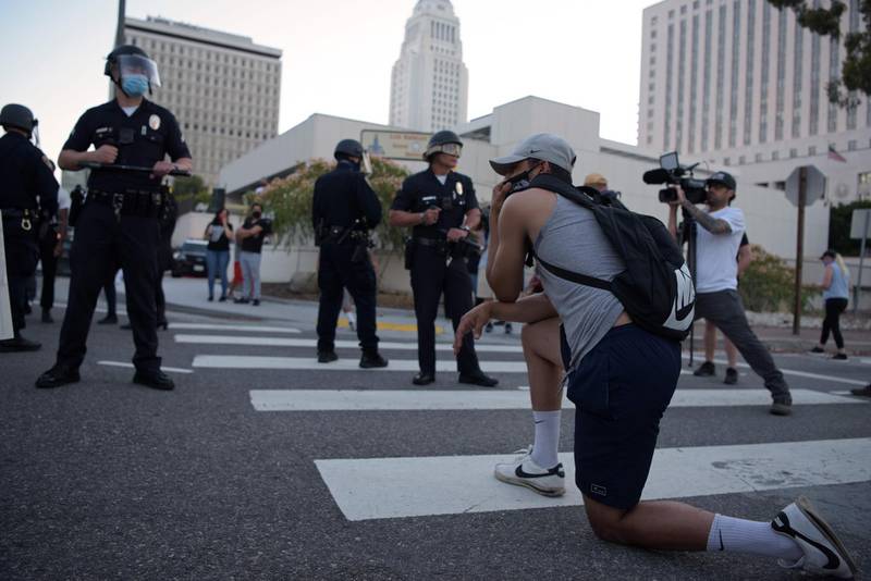 A demonstrator kneels in front of a row of police officers as protesters gather in downtown Los Angeles on May 27, 2020. AFP