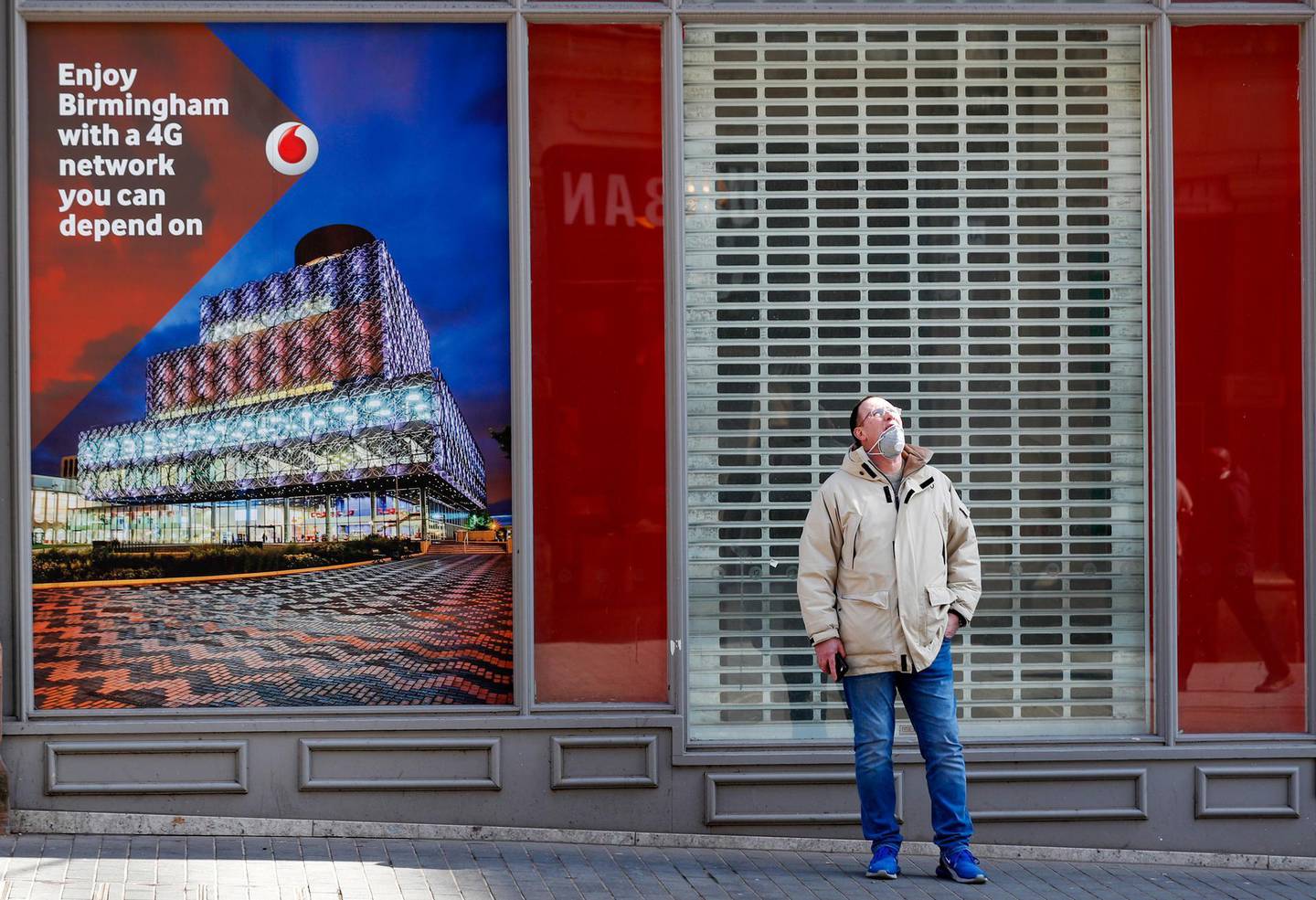 A pedestrian, wearing a protective face mask, stands outside a Vodafone Group Plc store near a advertising message about their 4G network in Birmingham, U.K., on Monday, April 6, 2020. Telecom masts that enable the next generation of wireless communication were set on fire in the U.K. in recent days, apparently by people motivated by a theory that the tech helps spread the coronavirus. Photographer: Darren Staples/Bloomberg