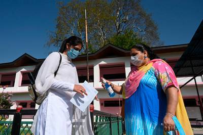 A teacher sprays sanitiser on the hands of student entering a school in Srinagar. AFP