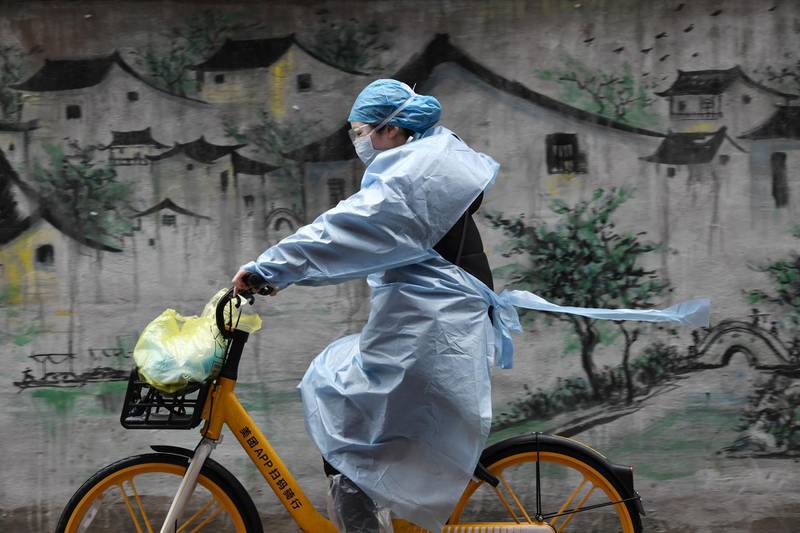A woman in protective gear rides a shared bicycle past a mural in Wuhan, the epicentre of the novel coronavirus outbreak, Hubei province, China. Reuters