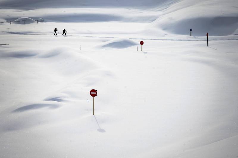 Two skiers pass by traffic signs submerged in thick snow at a car park near La Dole in the Swiss Alps. AFP