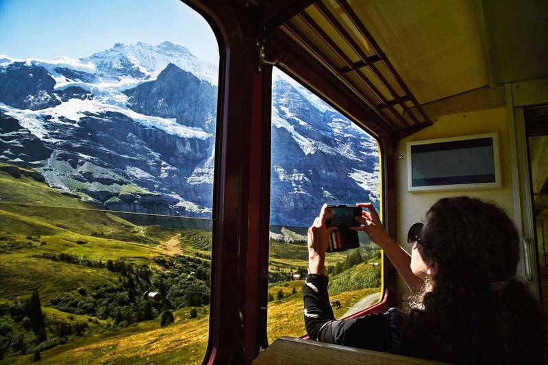 Woman taking photo with smartphone of Jungfrau while riding in train. Getty Images