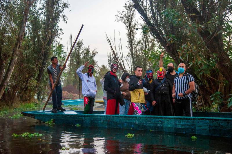 Wrestlers gesture from a typical 'trajinera' (boat), on arrival at the Chinampalucha event organized by Mexican wrestlers in the chinampas of Xochimilco in Mexico City as rings remain closed due to the Covid-19 coronavirus pandemic. AFP