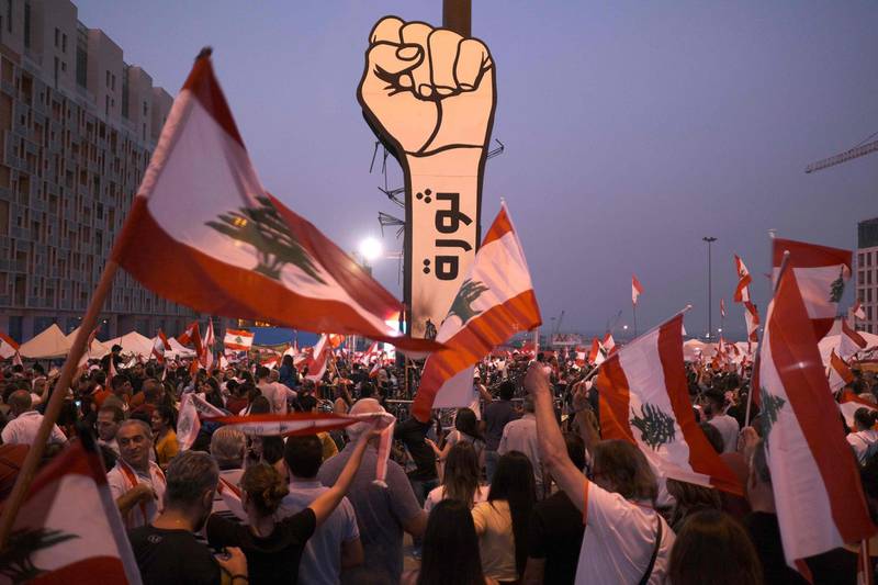 This picture taken on November 10, 2019 shows protesters waving Lebanese national flags by a giant sign of a fist with the slogan "revolution" written on it in Arabic in the capital Beirut's Martyrs' Square during continuing anti-government protests.  / AFP / Amir Makar                                                                                                                                                                                                                                                     

