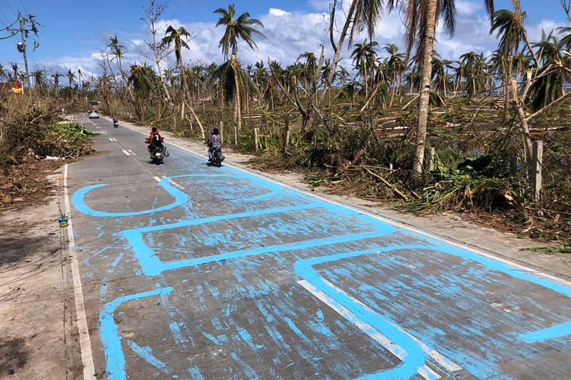 Motorists drive past signs asking for help painted on a road in General Luna town. AFP