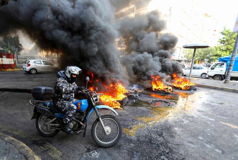 A Lebanese policeman rides his motocycle passed a road, blocked by anti-government protesters with burning tyres, in the capital Beirut.  AFP