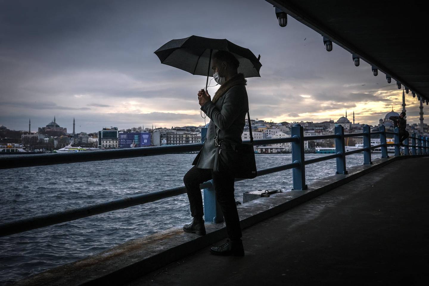 epa08910572 A man waits under the Galata Bridge with Hagia Sophia Mosque (L) and Yeni Mosque (R)  in the background on a rainy day, amid the ongoing coronavirus pandemic in Istanbul, Turkey, 28 December 2020. Turkey imposed curfews on weekdays after 9pm and full weekend lockdowns with the exception of tourists to combat the spread of coronavirus, after a recent spike in Covid-19 infections and related deaths.  EPA/SEDAT SUNA