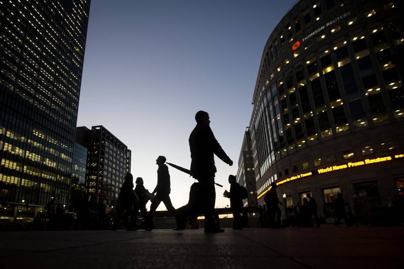 Commuters walk past the JP Morgan, left, and Thomson Reuters Corp., right, buildings illuminated at night in the Canary Wharf business, financial and shopping district of London, U.K., on Wednesday, Oct. 28, 2015. In its monthly consumer confidence index, GfK said a measure of Britons' outlook for the economy over the next 12 months dropped to minus 4 in October, the lowest reading this year. Photographer: Simon Dawson/Bloomberg