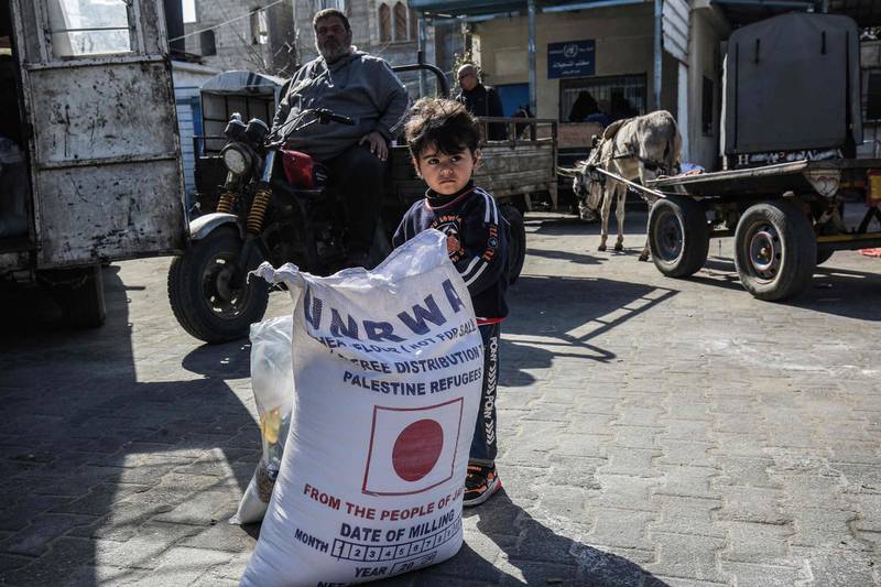 A child stands next to a sack flour as people come to receive food aid from a United Nations Relief and Works Agency (UNRWA) distribution centre in the Khan Yunis camp for Palestinian refugees in the southern Gaza Strip on February 2, 2020.  / AFP / SAID KHATIB
